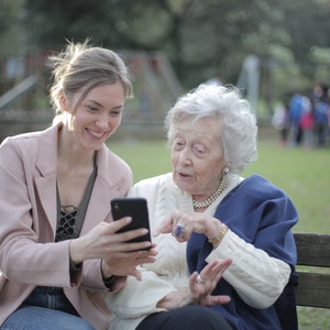 Girl showing something from the phone to elderly woman.